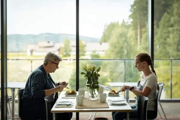 To voksne damer spiser lunsj i museumsbygningen med utsikt til langhuset