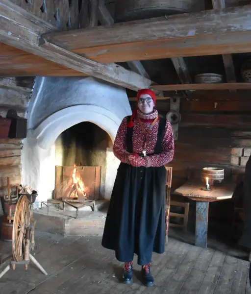 Bilde inne i Sørhovstua fra Rollag. Vi ser en museumsvert, en rokk et bord og peisen bak.