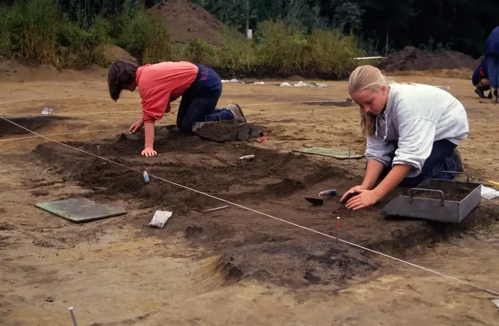 To ungdom fra er med på arkeologisk utgravninger. De graver i bakken.