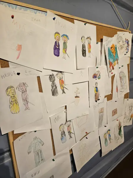 En oppslagstavle med mange tegninger, fargelagt av barn. Tegningene viser barnekarakterene Idun og Isak, og viser frem en aktivitet for barn hvor oppgaven er å fargelegge disse to figurene.