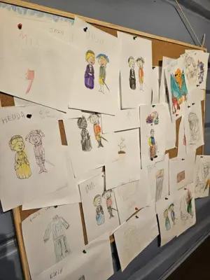 En oppslagstavle med mange tegninger, fargelagt av barn. Tegningene viser barnekarakterene Idun og Isak, og viser frem en aktivitet for barn hvor oppgaven er å fargelegge disse to figurene.