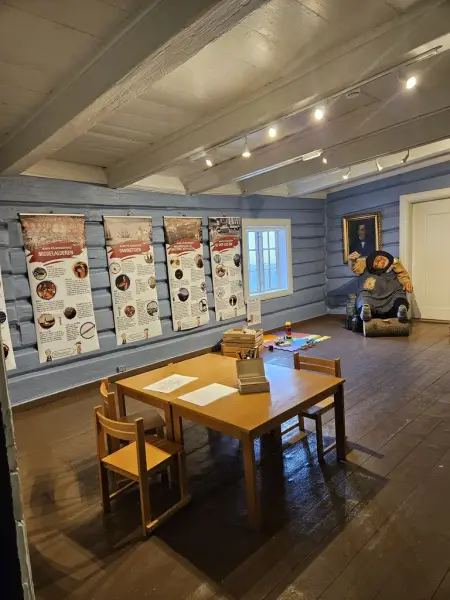 Et rom med blå vegger og flere informasjonstavler. Et bord og stoler er plassert midt i rommet, med fargestifter og en skattekiste.I bakgrunnen ser man ulike aktiviteter og leker, samt en stor dukke av et troll. 