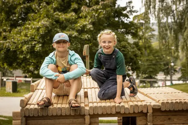 To barn som sitter på en laftet minibygning. Bygningen er satt sammen av et leikelaftesett.