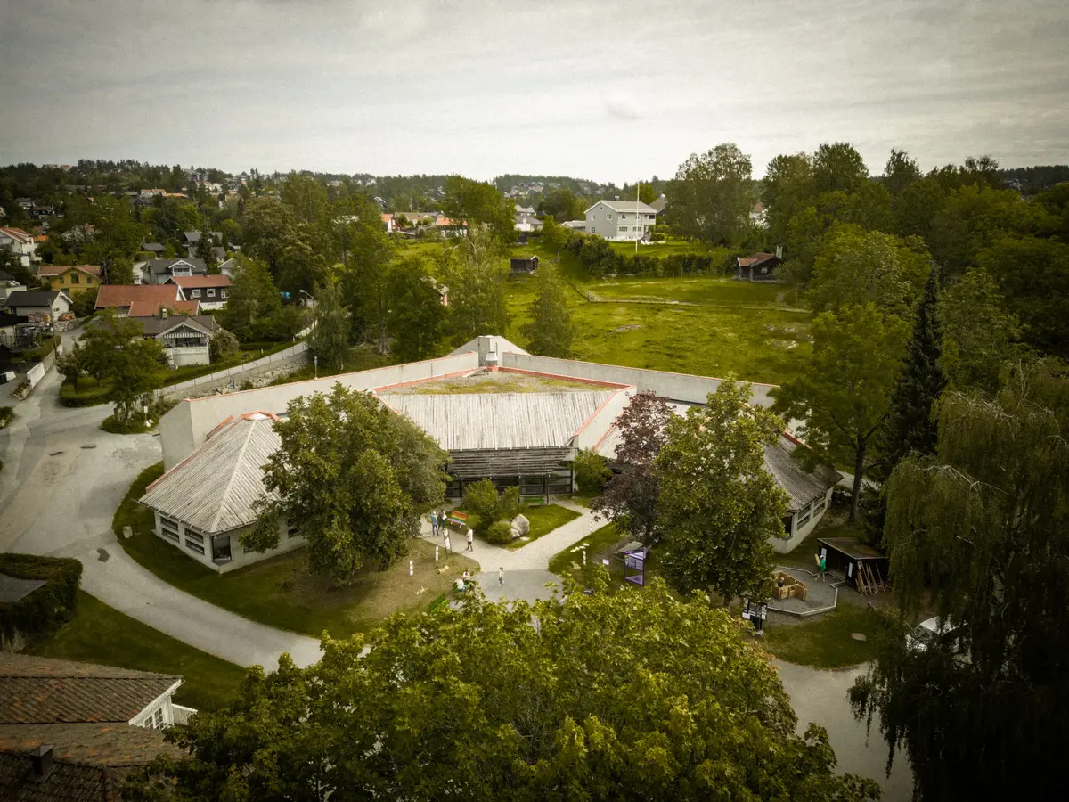 Bilde av hovedbygningen på Lågdalsmuseet. Bildet er tatt av drone og viser bygningen ovenifra. Vi ser publikum ute på plassen foran hovedbygningen. 