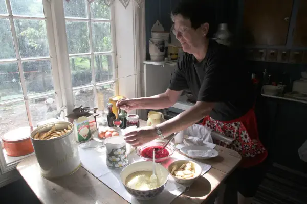 På bildet ser vi en av venneforeningens medlemmer servere tradisjonsmat. På bordet står det småkaker, syltetøy, salt, egg, med mer.