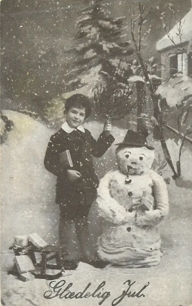 En gutt og en snømann i et snødekket landskap og teksten "Glædelig jul"