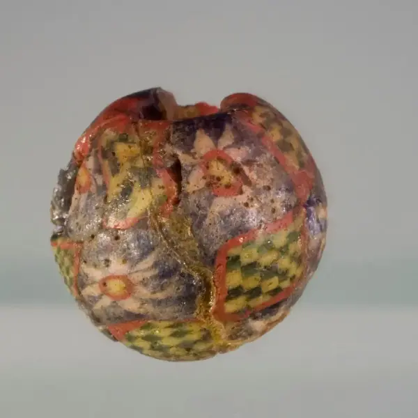 Mosaikkperle med fargene blå, rød hvit, gul og grønn. Noe sjakkmønster i fargene gult og grønt. Blomster som er hvite, røde og gule i midten og blå bakgrunn. 