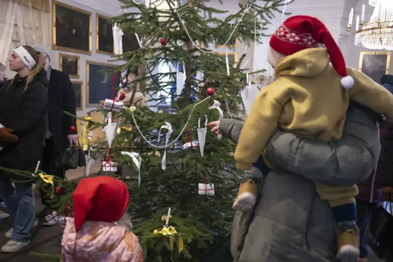 En kvinne og to barn ser på et pyntet juletre. 