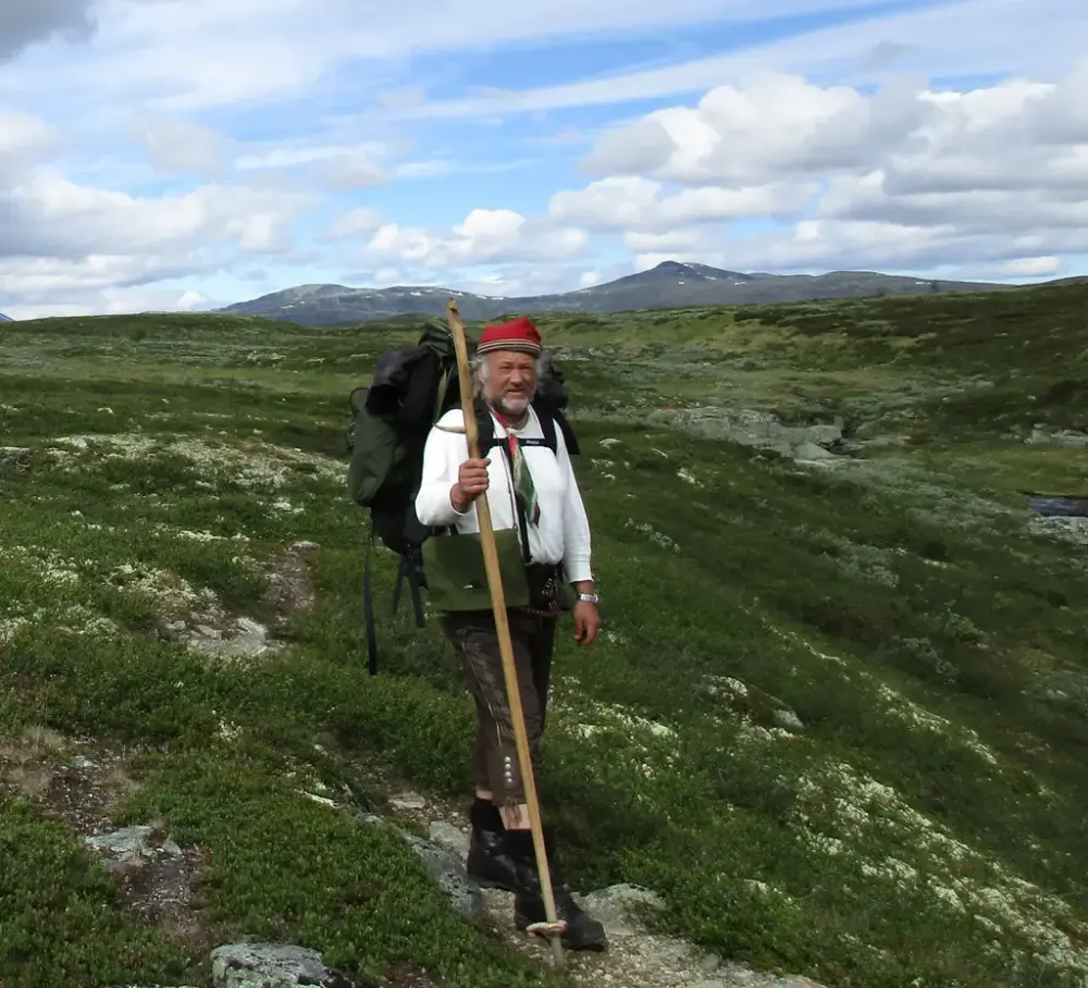 Mann med sekk på ryggen og vandrestav i hånden i høyfjellet