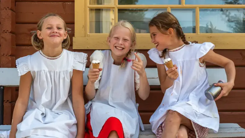 Tre jenter i hvite kjoler som sitter forran en rød vegg