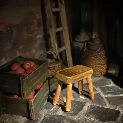 Foto av detalj fra diorama i utstillingen "Skyggesider". Et rom med murvegger og steingulv. En krakk står foran tre kasser med epler. Bak krakken er to kurver og en stige.
