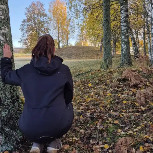 Arkeolog sitter på huk og ser på Kongshaugen, den største gravhaugen på Veien. Det er høst og blader på bakken