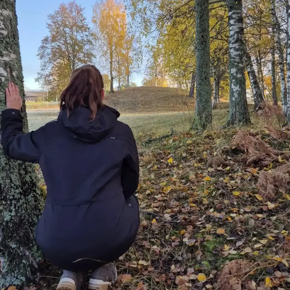 Arkeolog sitter på huk og ser på Kongshaugen, den største gravhaugen på Veien. Det er høst og blader på bakken