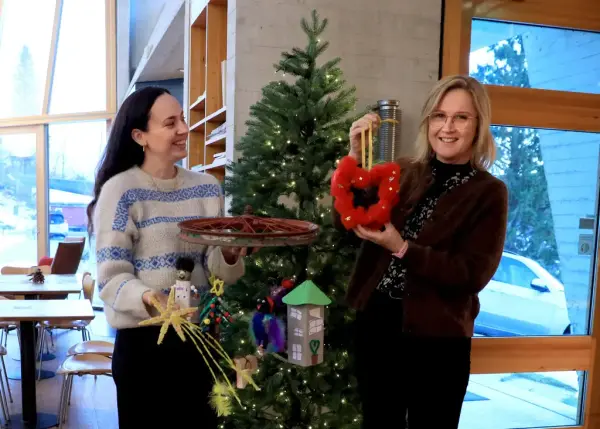 To personar framfor eit juletre med fargerik barnekunst i hendene.