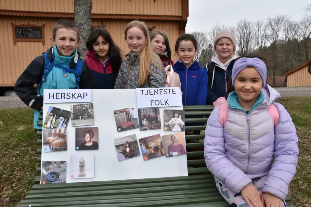 Skoleelever står ved siden av en plakat om herskap og tjenestefolk. 