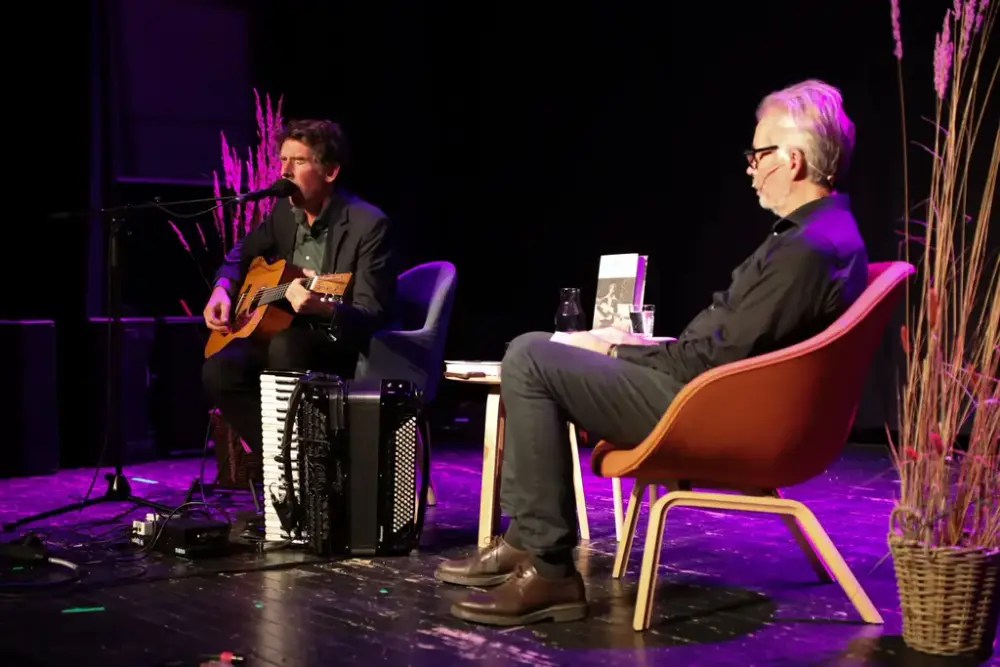 Scene med to stolar der Odd Nordstoga syng og spelar gitar medan Yngve Knausgård lyttar.