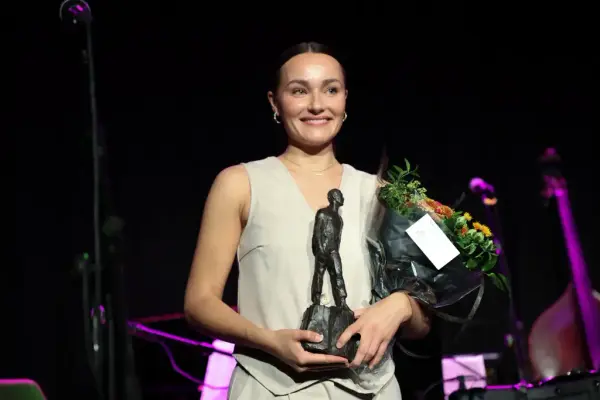 Smilande prisvinnar med blomar og statuett