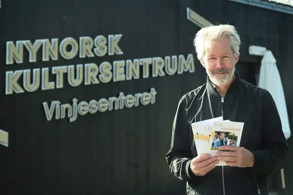 Bilete av ein smilande arenaleiar framfor Vinjesenteret med ei vifte av programhefte i hendene.