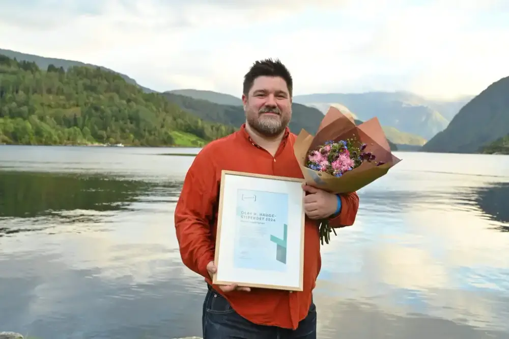 Poet Martin Ingebrigtsen med diplom og blomebukett med fjorden som bakgrunn.