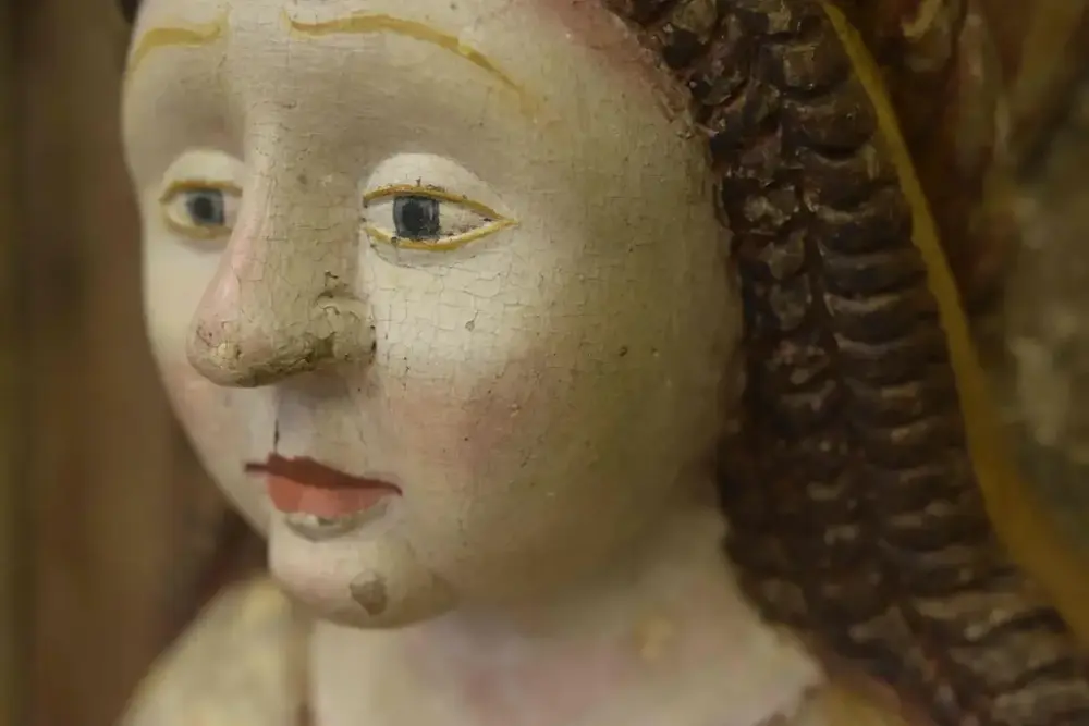 Målad staty där färgflagnor lossnat på medeltida kvinna.