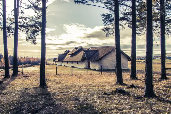 vårbilde av langhuset. Huset er 47 meter langt med hvite vegger, tre inngangsdører og 5 små vinduer. Taket er laget av planker.