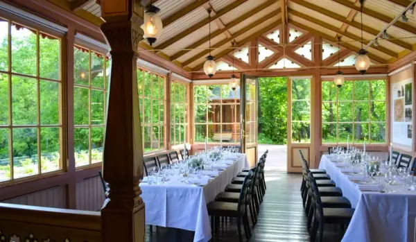 Sæterhytten ved Bygdø Kongsgård innenfra, to dekkede langbord med hvit duk og utsyn mot grønne trær.