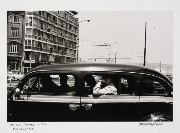 En sort og blank bil mot en bybakgrunn. Bilen har åpne vinduer og vi ser silhuetter av mennesker i bilen