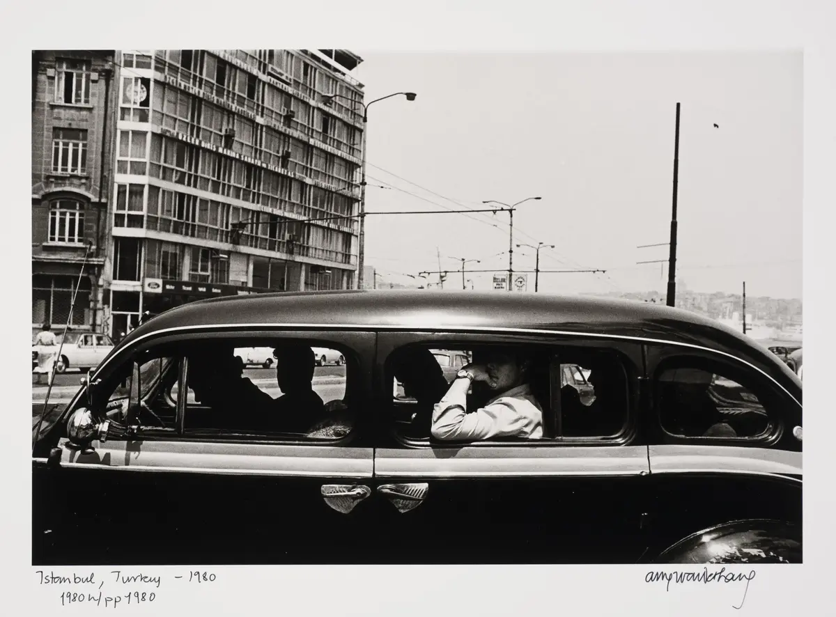 En sort og blank bil mot en bybakgrunn. Bilen har åpne vinduer og vi ser silhuetter av mennesker i bilen