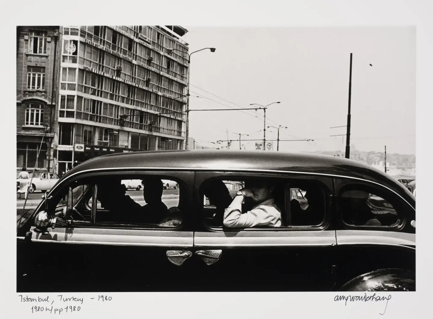 En sort og blank bil mot en bybakgrunn. Bilen har åpne vinduer og vi ser silhuetter av mennesker i bilen