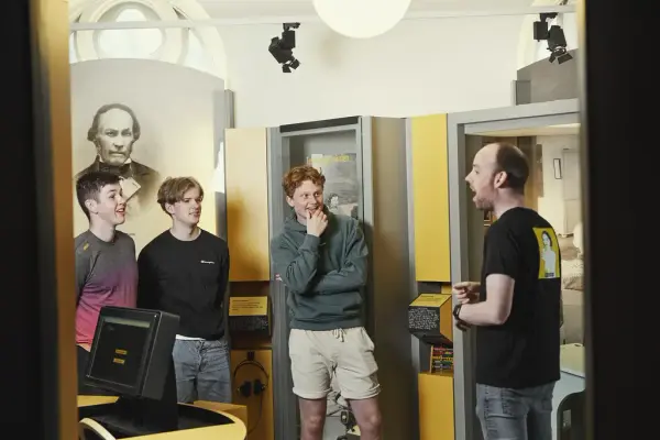 En mann snakker foran tre unge menn som lytter. Foto.