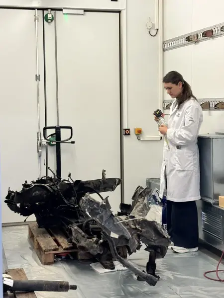 En ung kvinne iført hvit arbeidsfrakk ser ned på en brent og ødelagt gjenstand