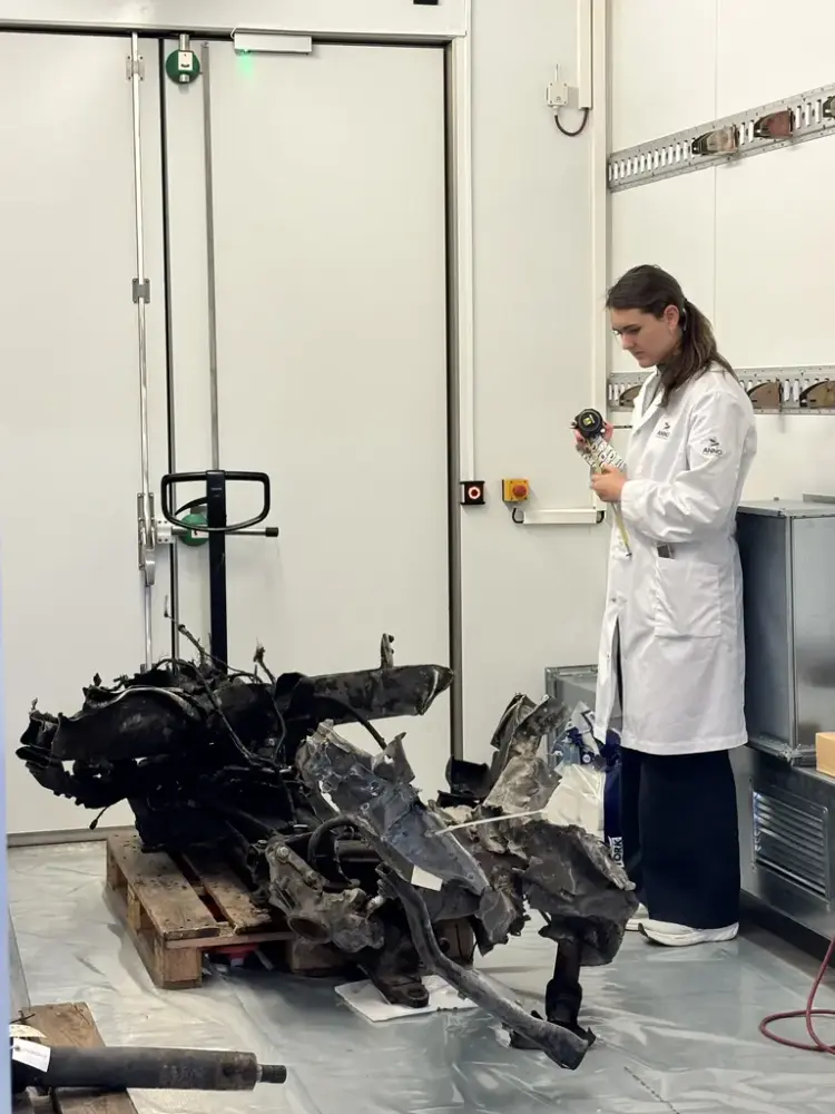 En ung kvinne iført hvit arbeidsfrakk ser ned på en brent og ødelagt gjenstand