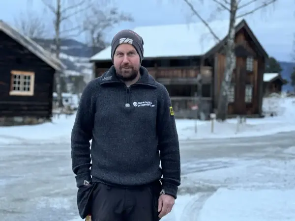manne med lue og grå genser foran snødekte gamle hus
