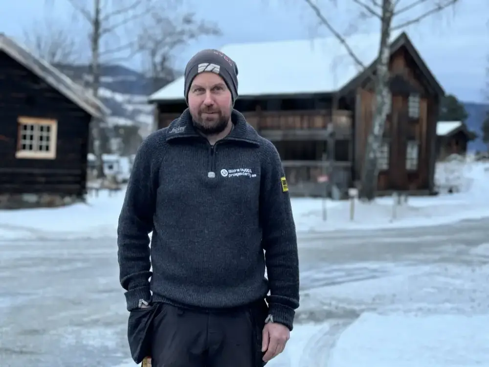manne med lue og grå genser foran snødekte gamle hus