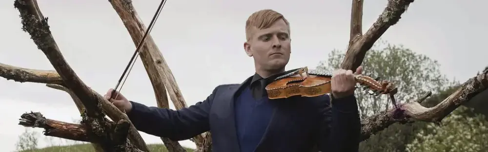 Erlend O Nødtvedt som spelar hardingfele med eit gammalt tre som bakgrunn