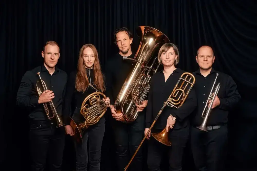 Gruppefoto av fem musikarar med instrument mot mørk scenebakgrunn.