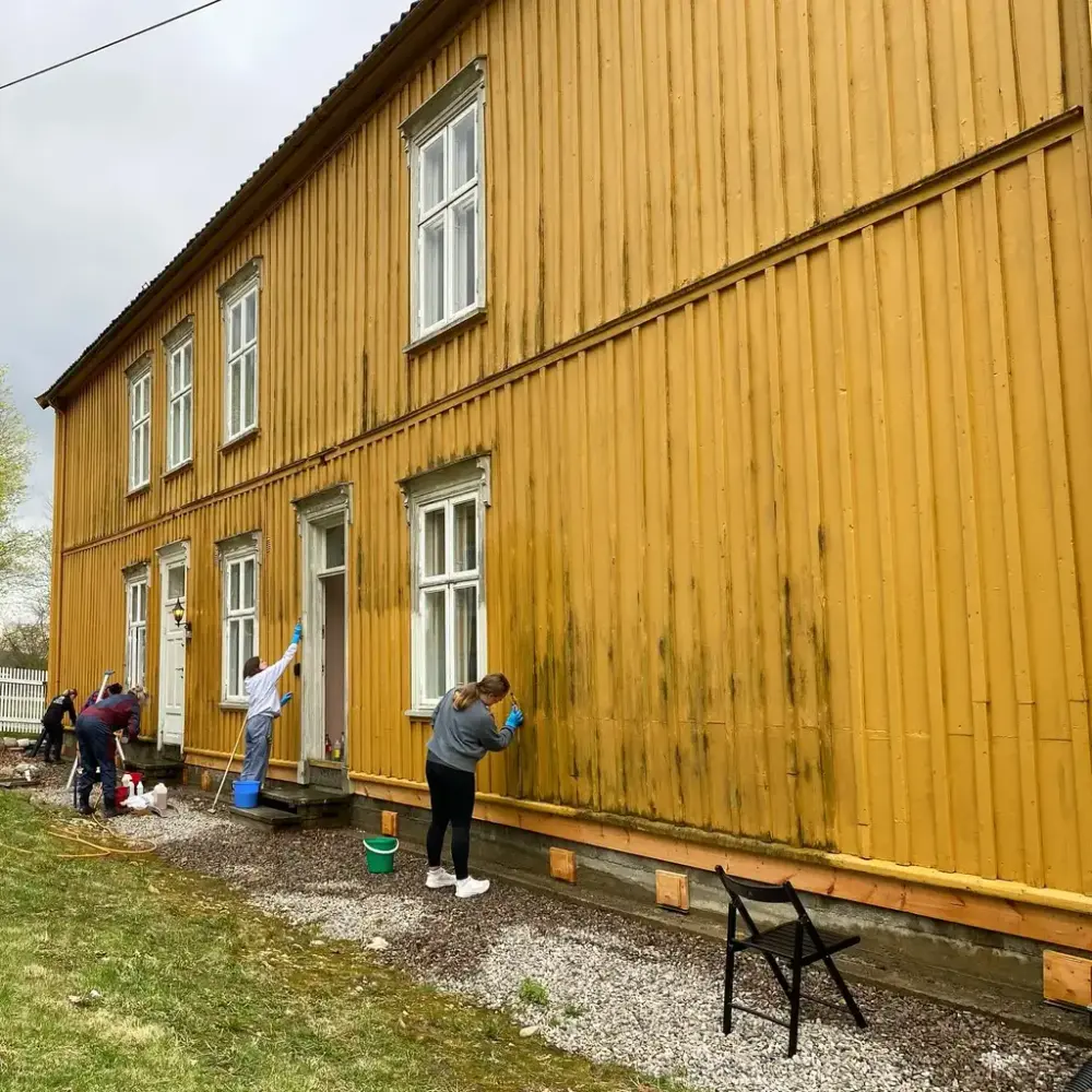 Fem personer vasker en skitten yttervegg på et gult bygg