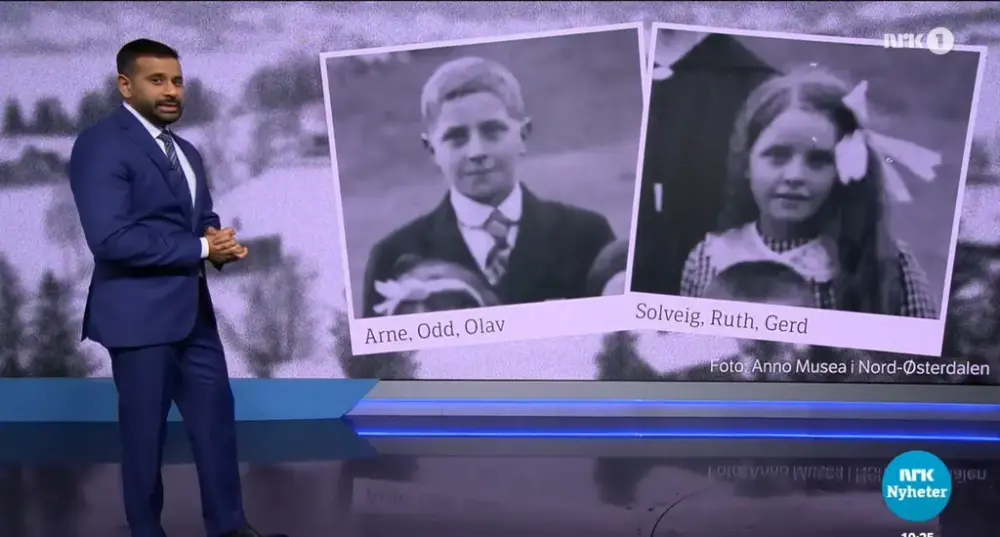 En mann iført en blå dress står foran en stor skjerm vor det blir vist to sort-hvitt bilder av en ung gutt og enn ung jente