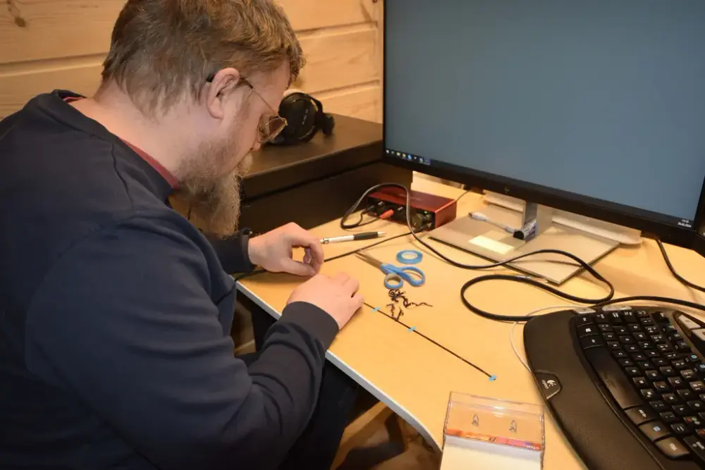 En mann sitter ved et skrivebord og teiper sammen et kassett-bånd