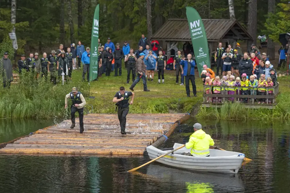 Publikum ser på når deltakere løper over flåte på vannet under utendørs arrangement.