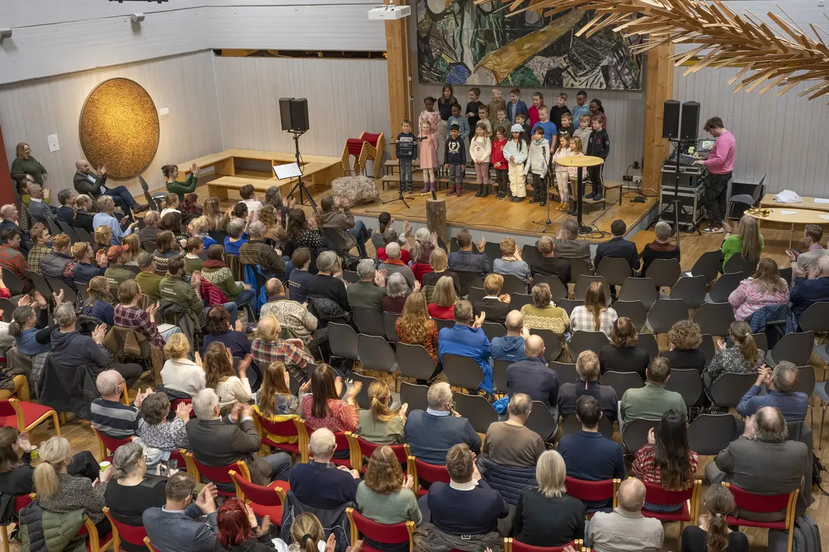 Fullsatt sal med publikum som ser barnekor opptre på scene.
