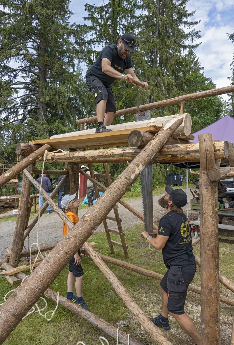 Personer bygger trekonstruksjon utendørs med stokker og tau.