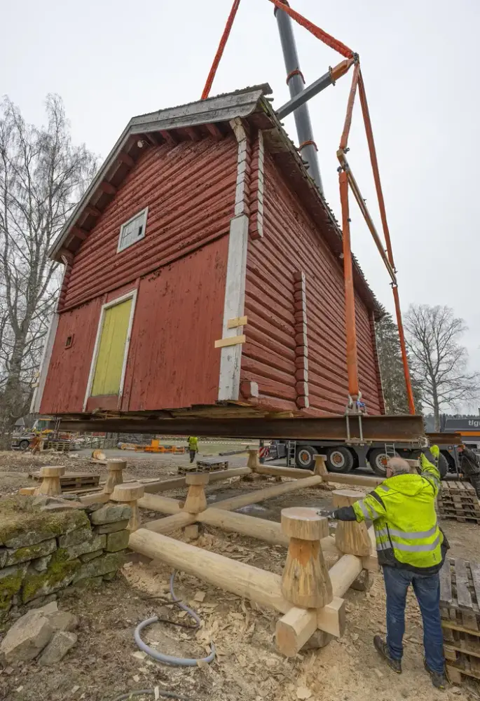 Lite rødt trehus løftes og flyttes ved hjelp av kran.