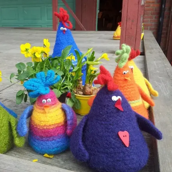 Fem fargerike høner i tovet ull sitter blant påskeblomster