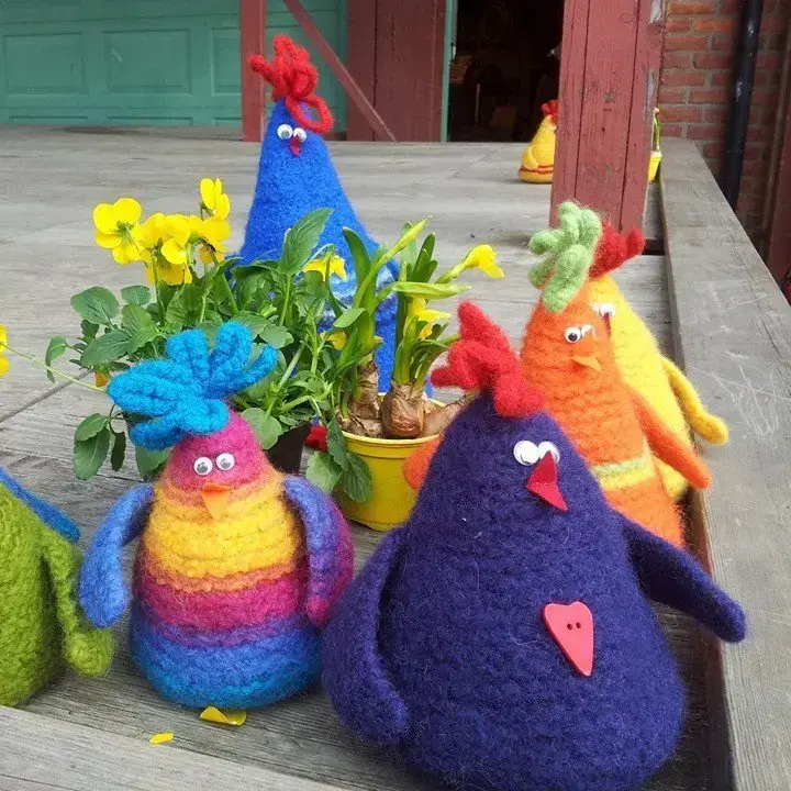 Fem fargerike høner i tovet ull sitter blant påskeblomster