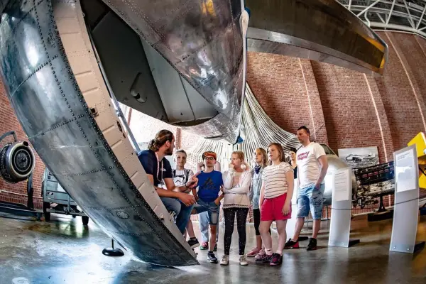 En omviser sitter under et fly og snakker med seks elever og to lærere