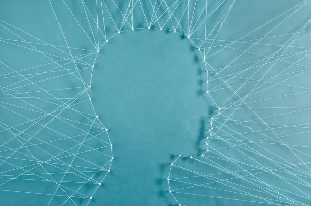 Illustrasjon med omriss av eit hovud i profil, danna av kvite trådar som er spente opp mellom stiftar. Turkis bakgrunn.