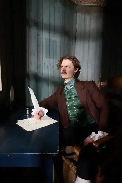 Mann i kostyme sitter ved skrivebord og holder en fjærpenn.