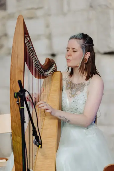 Ung kvinne i tyllkjole spiller harpe i domkirkeruinen.