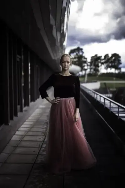 Portrett av sopran Ditte Marie Bræin i svart topp og rosa tyllskjørt, stående utendørs ved en moderne bygning før påskekonsert på Norsk Folkemuseum.
